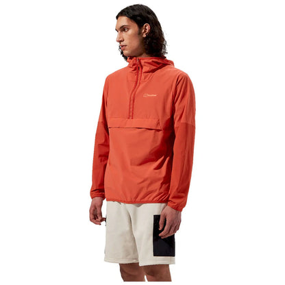 A young man wearing an orange hooded jacket stands sideways with a focused expression his left arm is slightly bent and he is wearing white shorts with black details against a plain white background