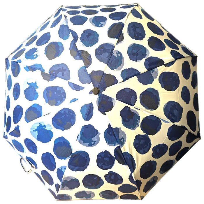 A round umbrella with a design of dark blue dots on a light background is opened and positioned upward, providing shade or protection from rain in an outdoor setting.