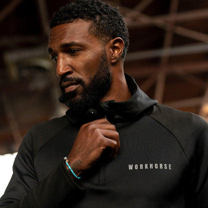 Man wearing Workhorse's High Collar Training Hoodie with logo in an industrial setting background.