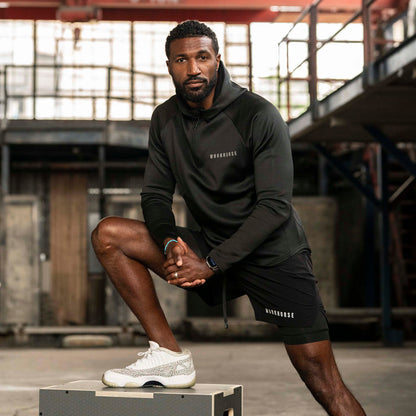 Man wearing Workhorse's High Collar Training Hoodie in black posing in an industrial setting