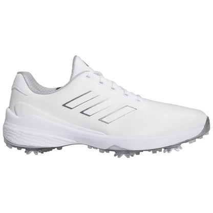 A white athletic shoe features three silver stripes on the side with a textured upper and a rubber sole equipped with small spikes designed for traction on grass or turf surfaces.