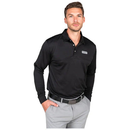 A man stands confidently wearing a long-sleeve black polo shirt and gray pants with one hand in his pocket showcasing a casual yet polished look against a plain background.